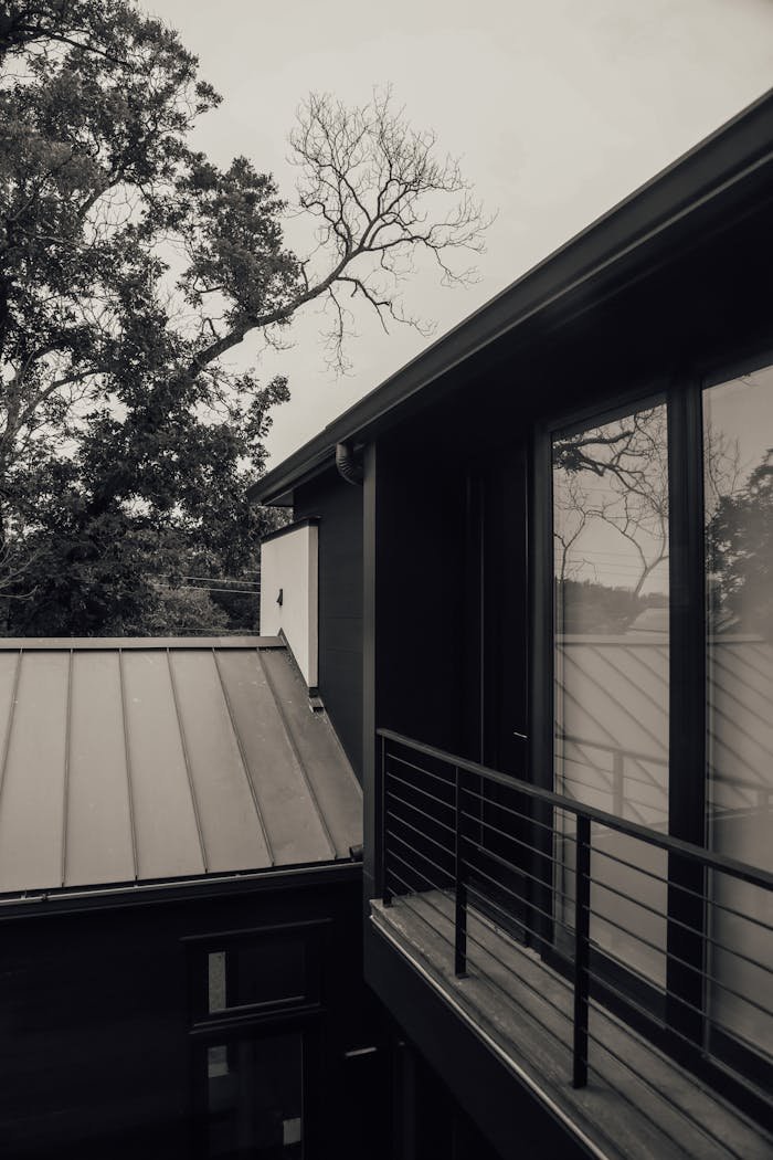 Black and white of small narrow open balcony of tall modern luxury house under leafless branches and gray sky