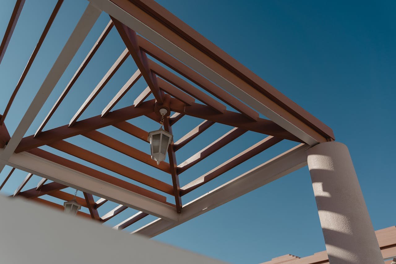 gallery-6 Low-angle view of geometric pergola structure with lanterns against a clear blue sky.
