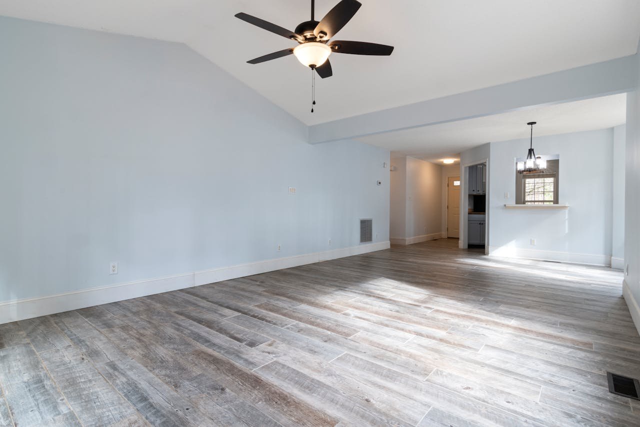 about-02 Bright and spacious empty living room with ceiling fan and wooden floor.